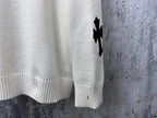 Light long-sleeve sweater with black cross detail and ribbed cuff