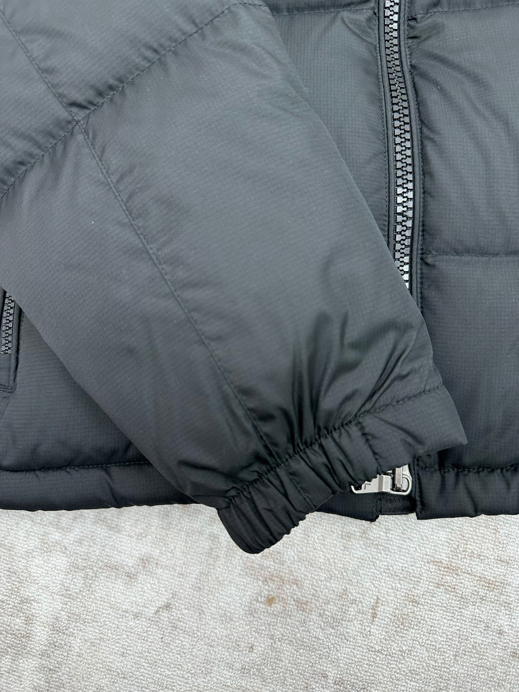 Dark puffer jacket sleeve cuff close-up with elastic hem and zipper trim