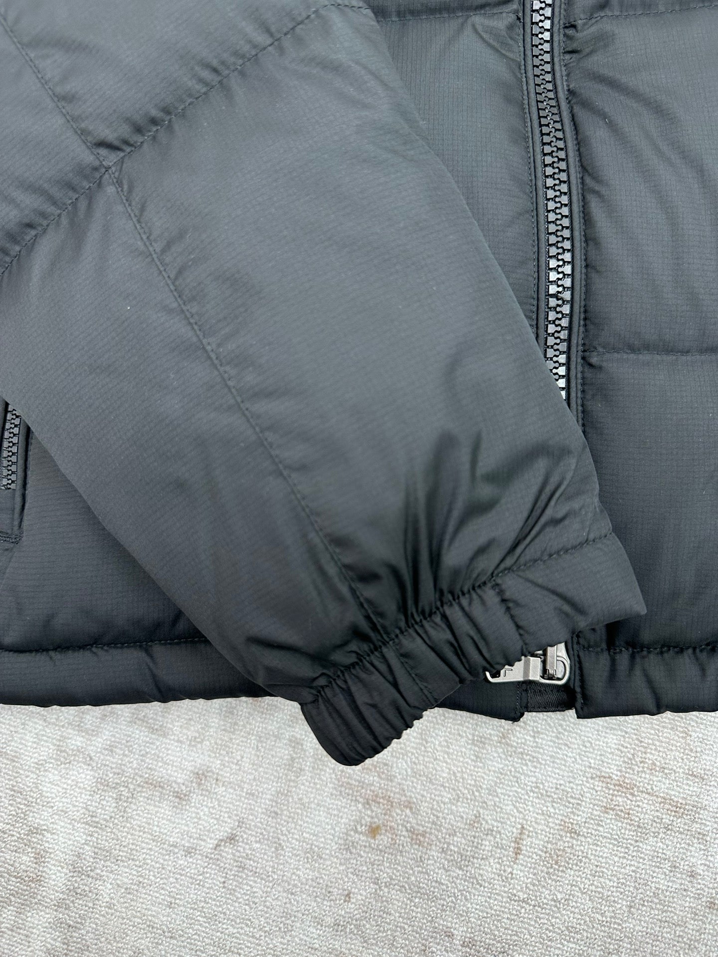 Dark puffer jacket sleeve cuff close-up with elastic hem and zipper trim