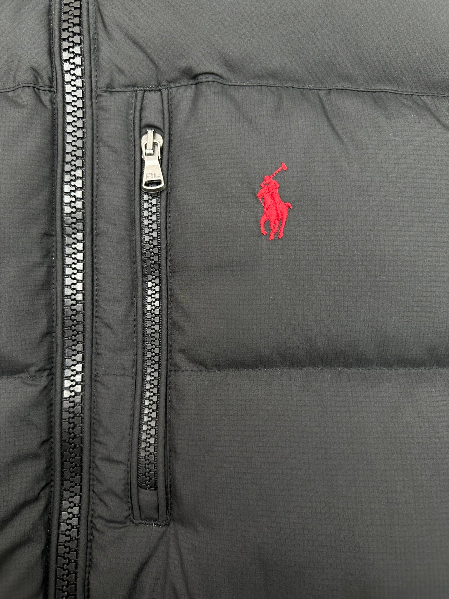 Dark puffer jacket front close-up with visible zip track and small red logo