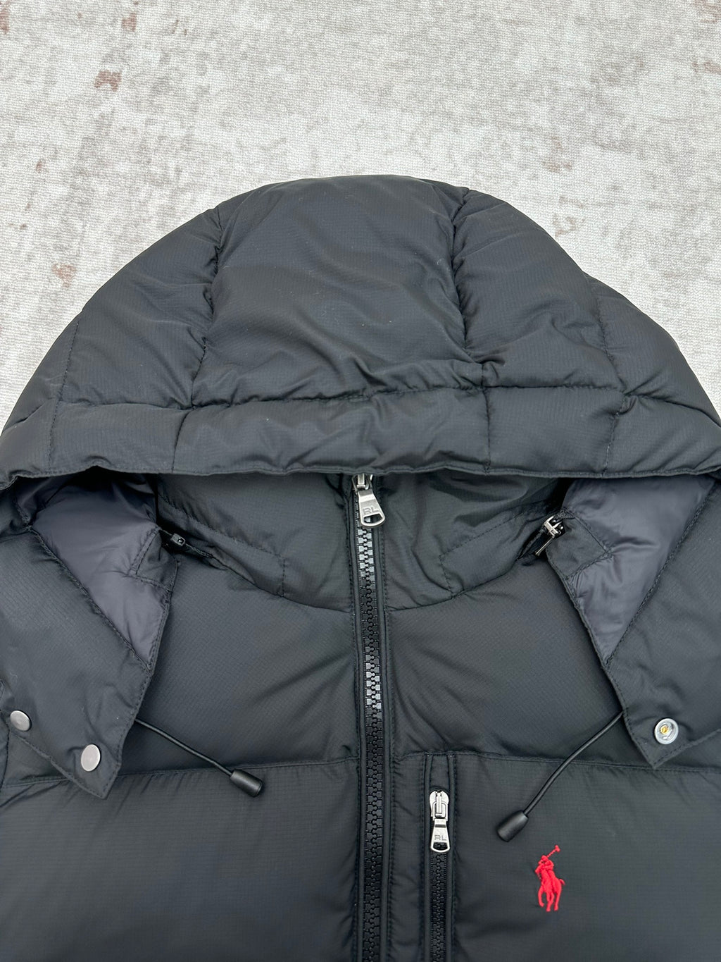 Dark puffer jacket close-up with full-zip and snap buttons, red logo on chest