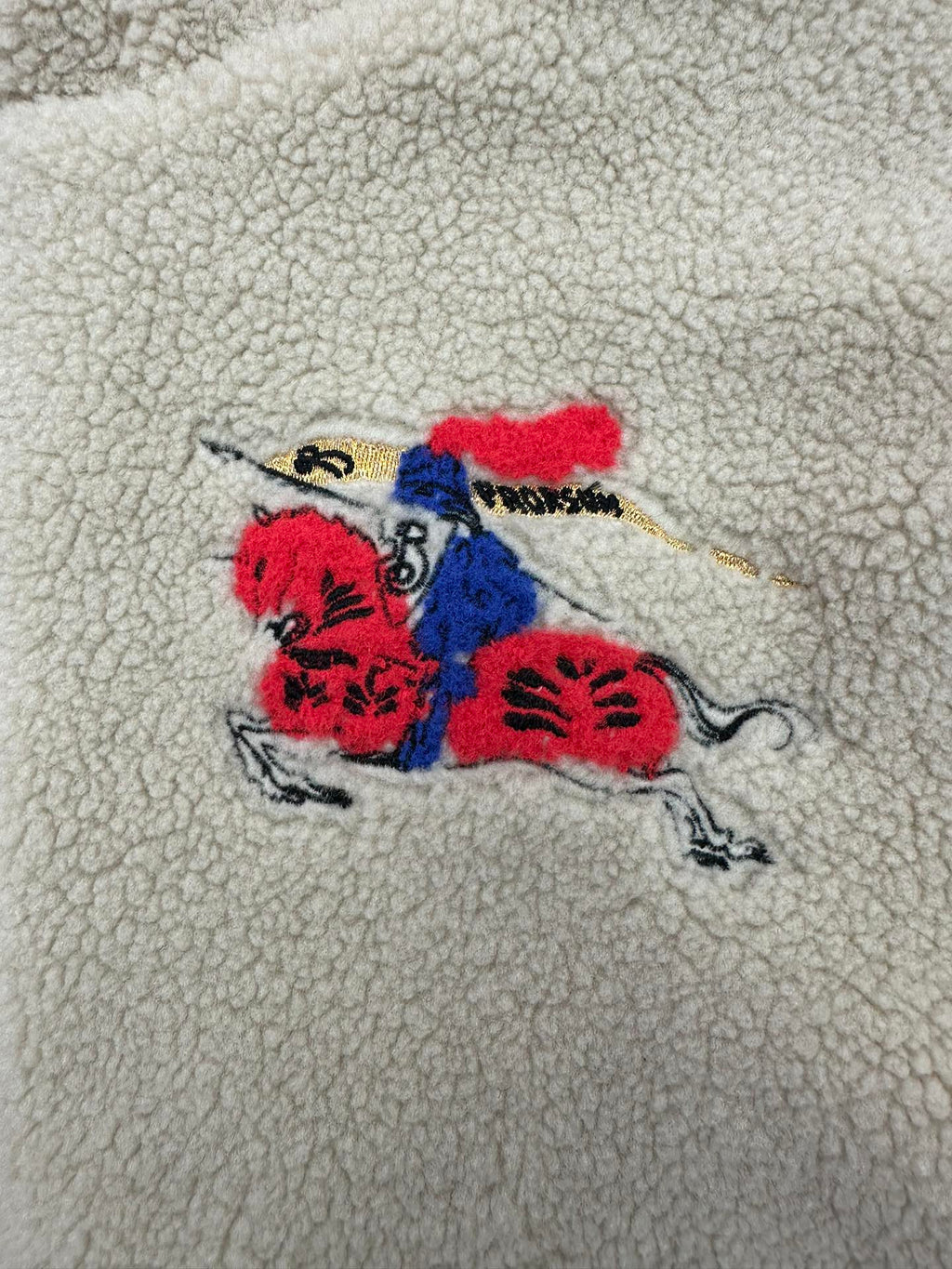 Colorful embroidered graphic on cream sherpa jacket: red, blue and black motif