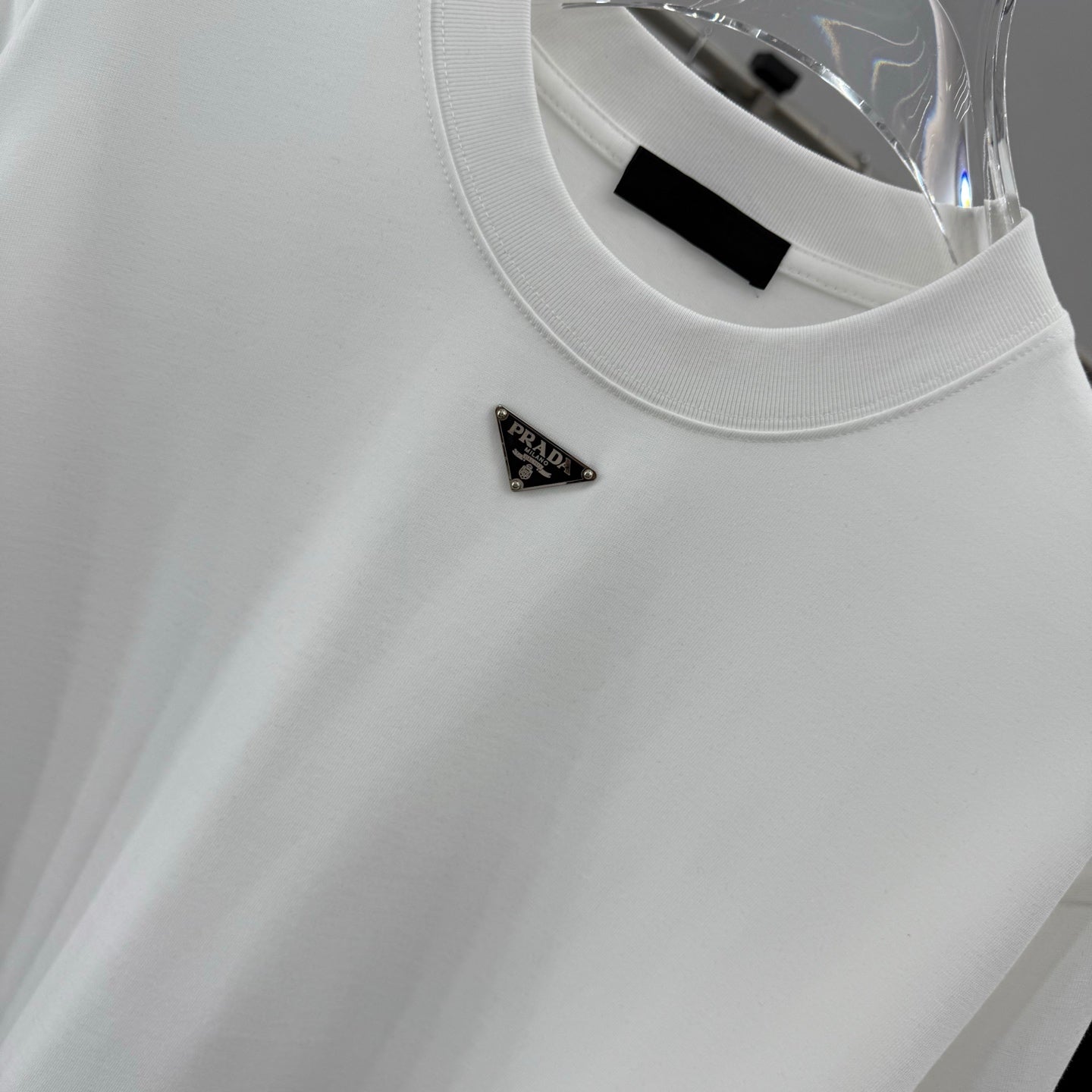 White T-shirt with Prada triangular metal logo pin on the chest