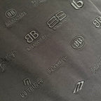 Black fabric close-up with raised tonal logo pattern and monograms