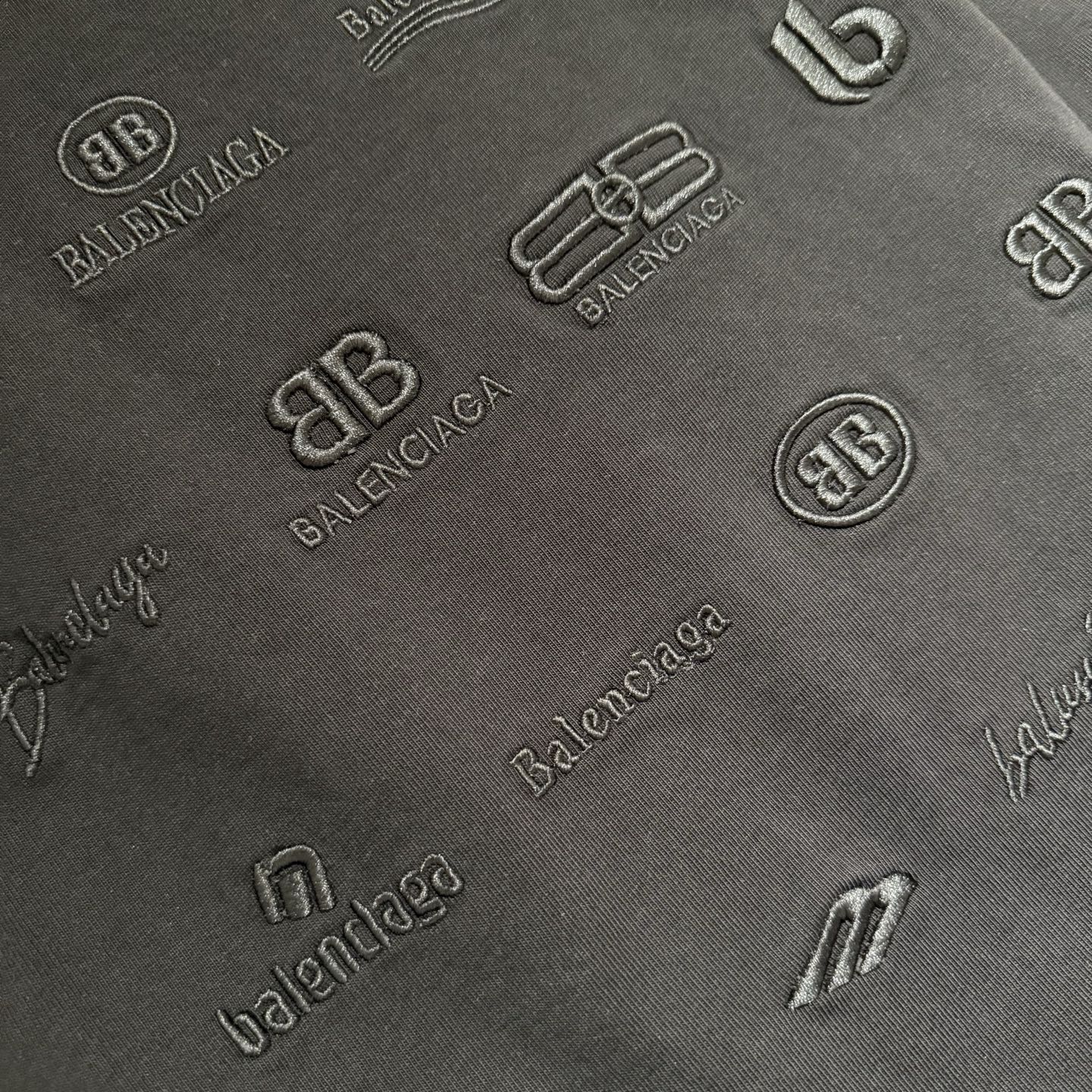 Black fabric close-up with raised tonal logo pattern and monograms