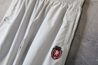 White wide-leg pants with embroidered crest patch and curved logo mark
