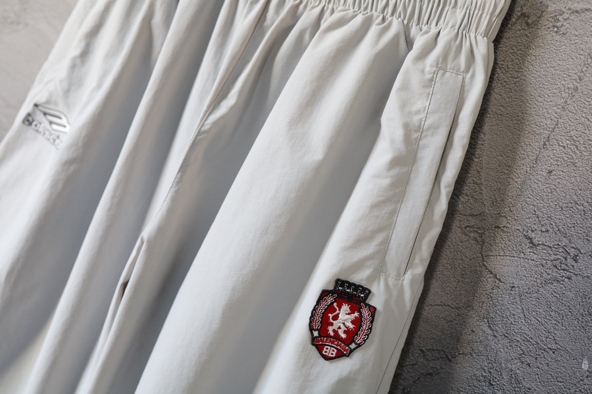 White wide-leg pants with embroidered crest patch and curved logo mark