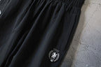 Black Balenciaga pants with gathered hem and side crest patch detail