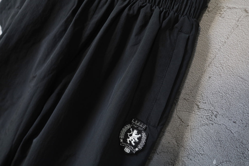 Black wide-leg pants with side crest patch and textured fabric panel