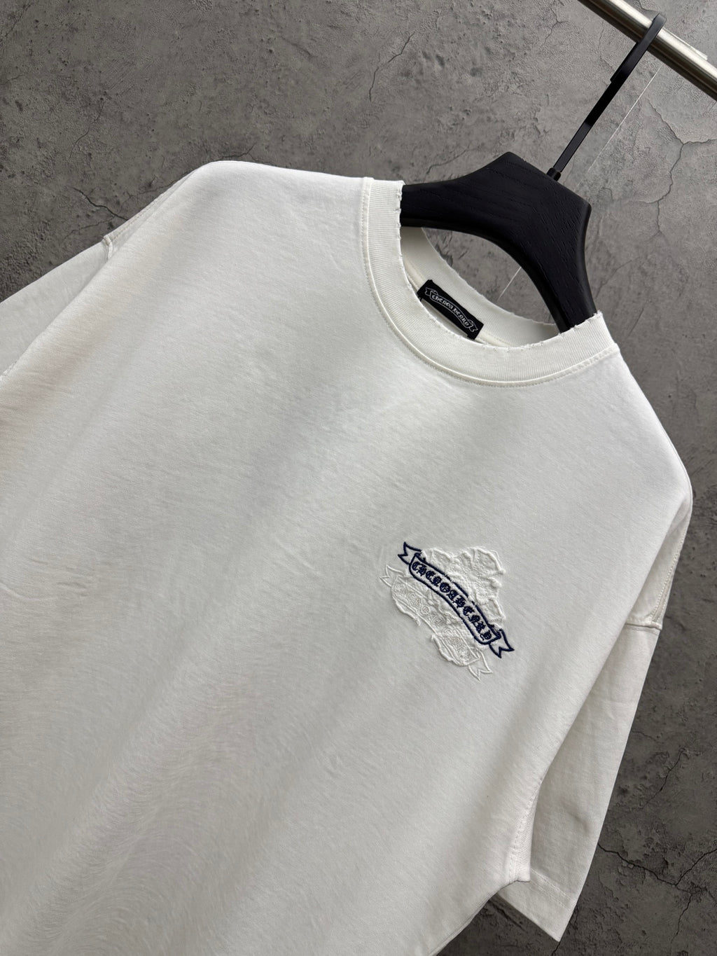 White short-sleeve T-shirt close-up at neckline with small blue logo embroidery on chest