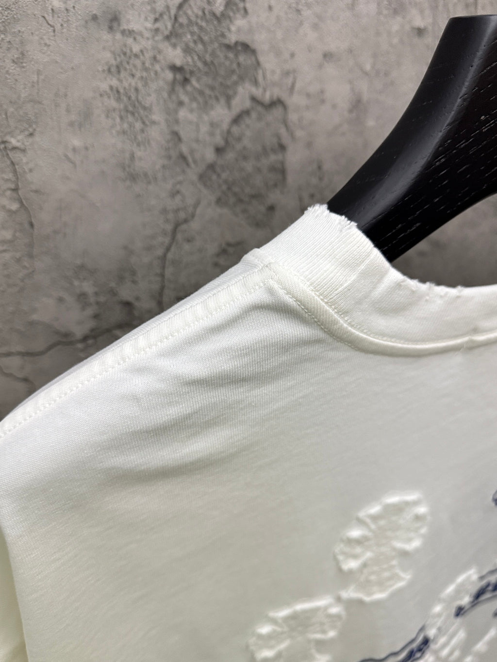 White short-sleeve T-shirt shoulder and collar seam with raised applique detail near hem