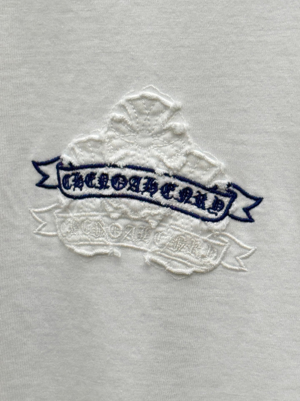 White short-sleeve T-shirt close-up of blue banner text with raised stitched snowflake texture
