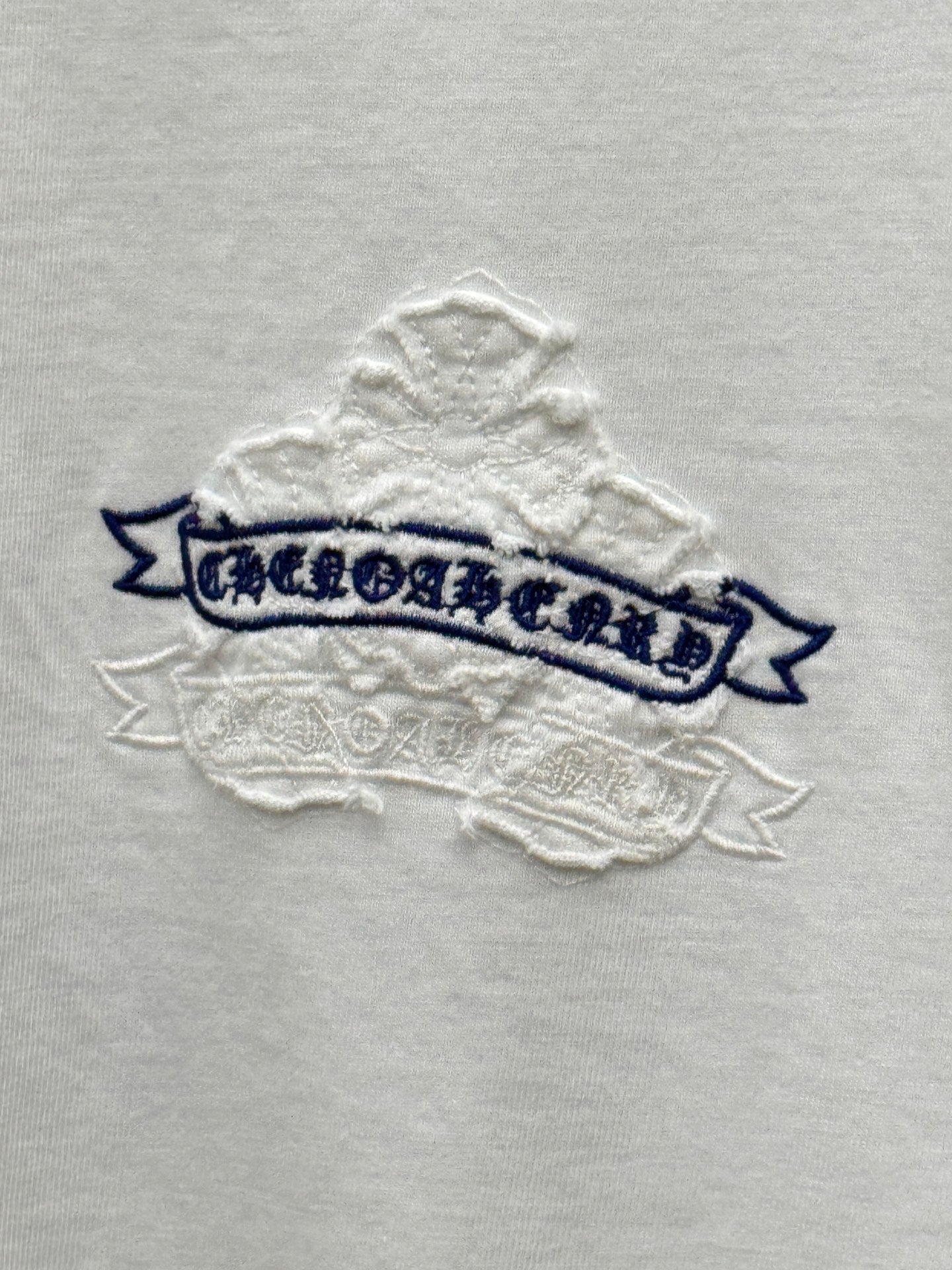 White short-sleeve T-shirt close-up of blue banner text with raised stitched snowflake texture
