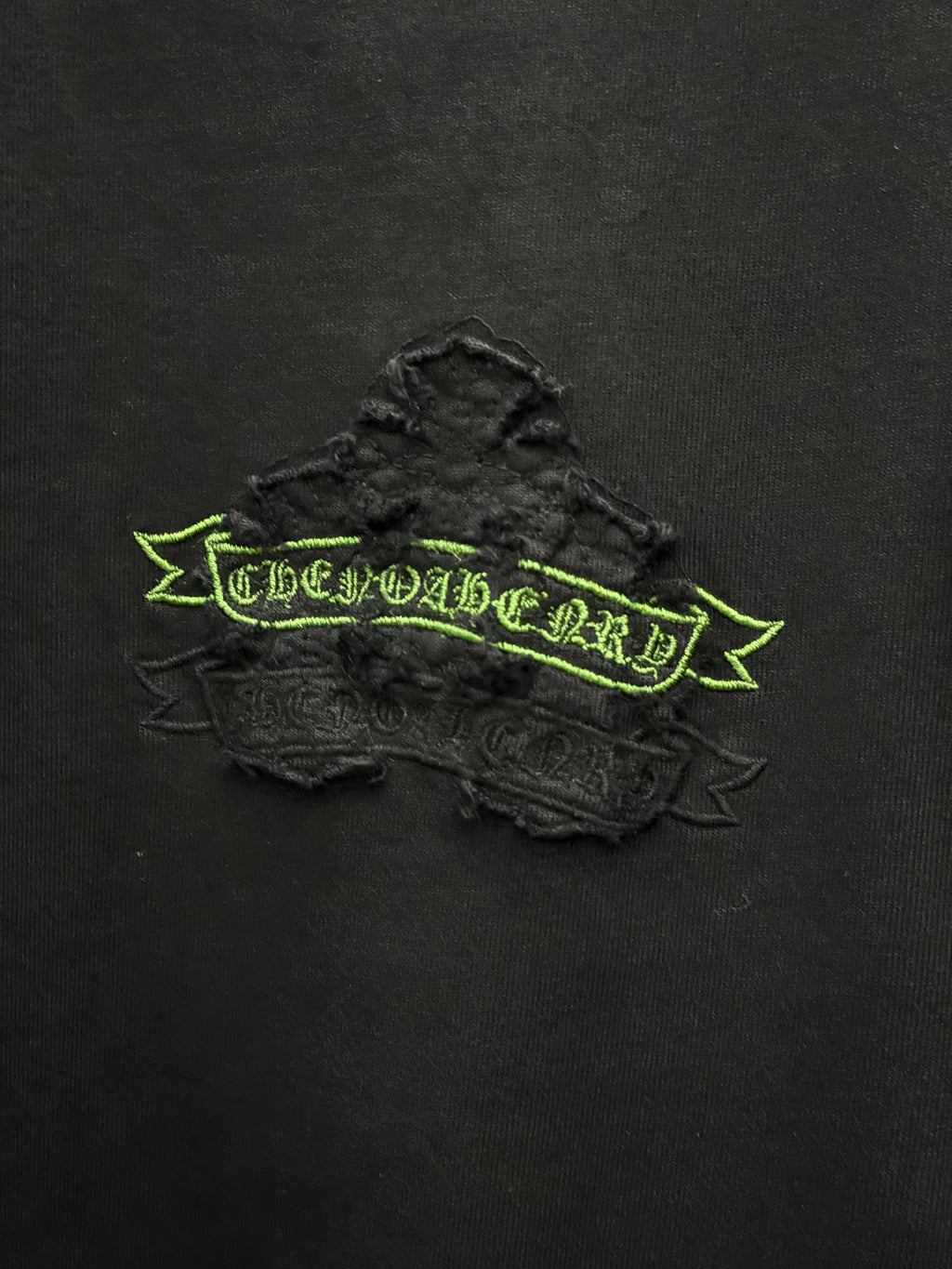 Black short-sleeve T-shirt close-up of raised green embroidered logo banner