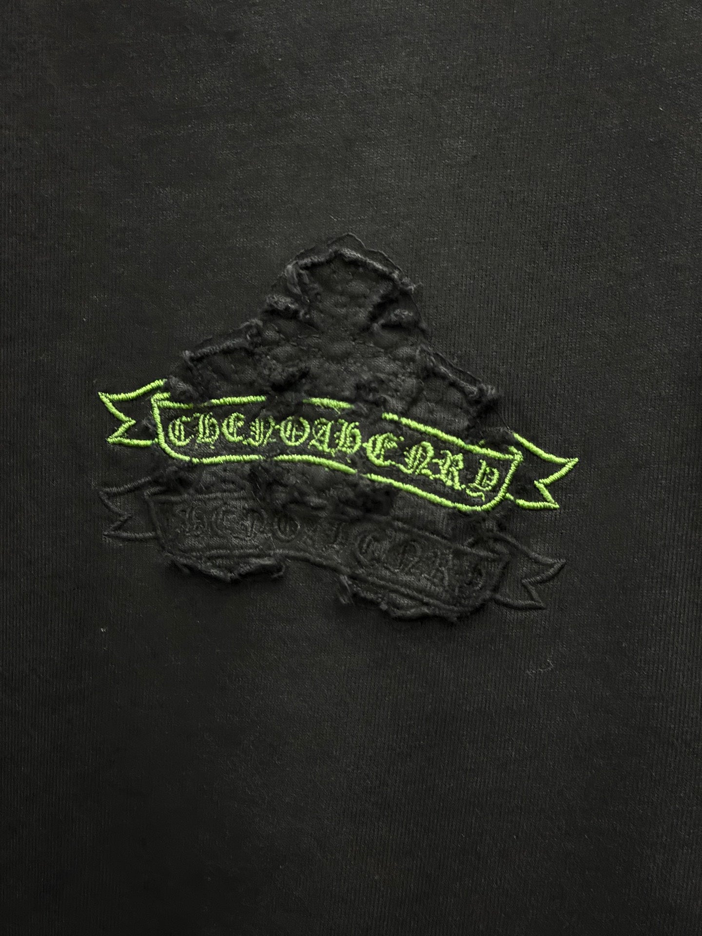 Black short-sleeve T-shirt close-up of raised green embroidered logo banner