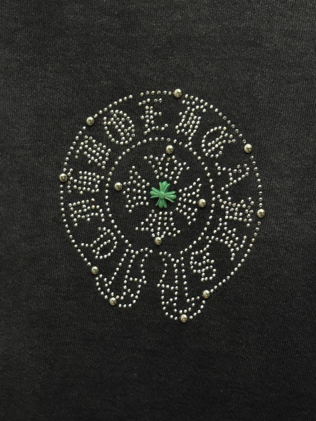 Round studded emblem detail on dark T-shirt with small green star center