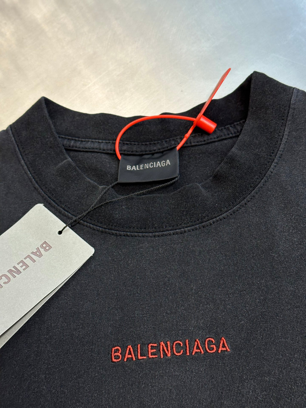 Dark gray crewneck T-shirt with red Balenciaga logo and hanging neck tag