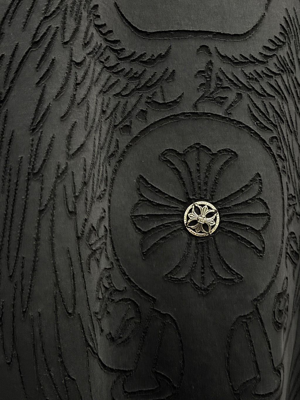 Close-up of embossed winged emblem with gold center on dark t-shirt