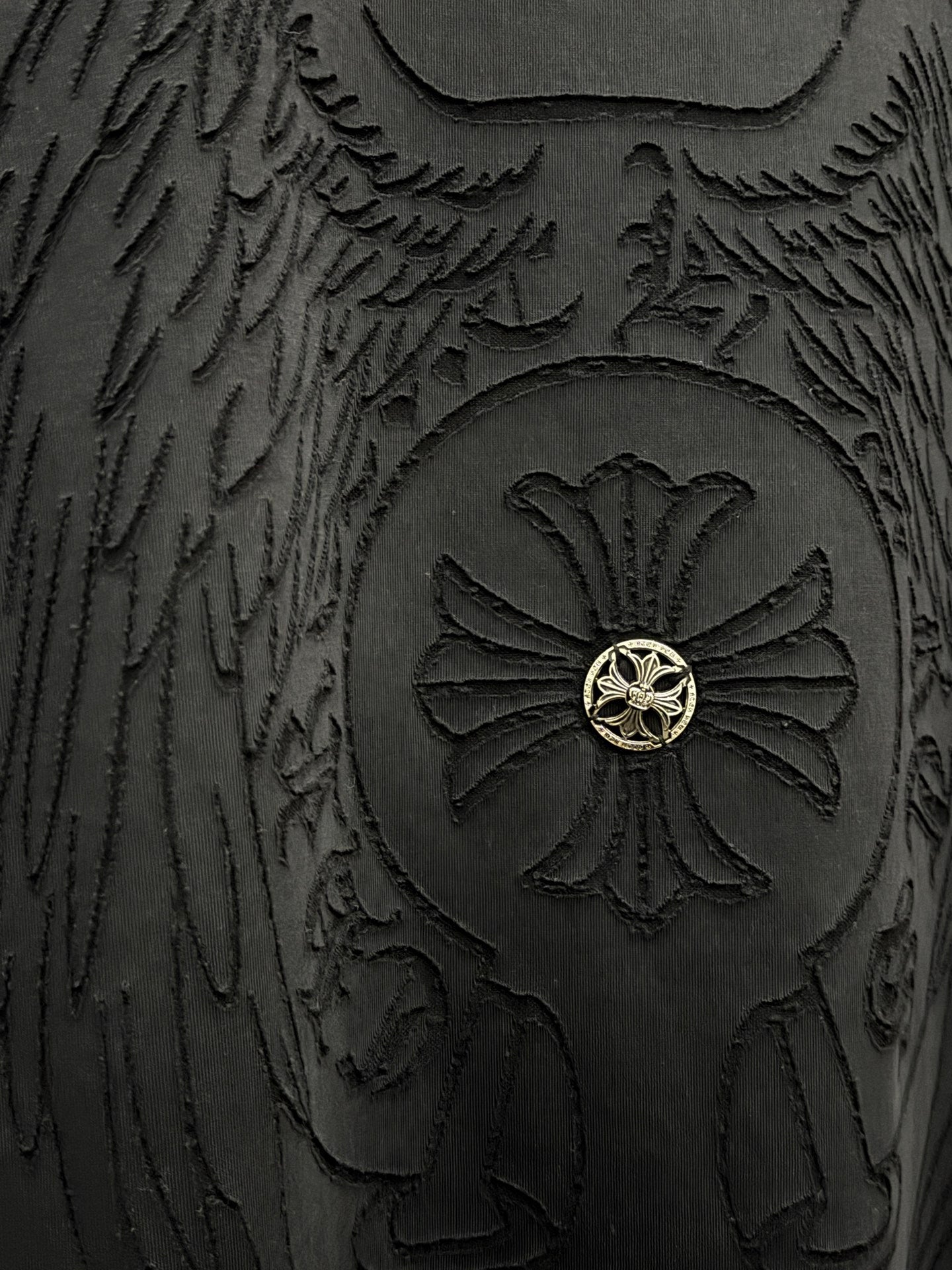 Close-up of embossed winged emblem with gold center on dark t-shirt