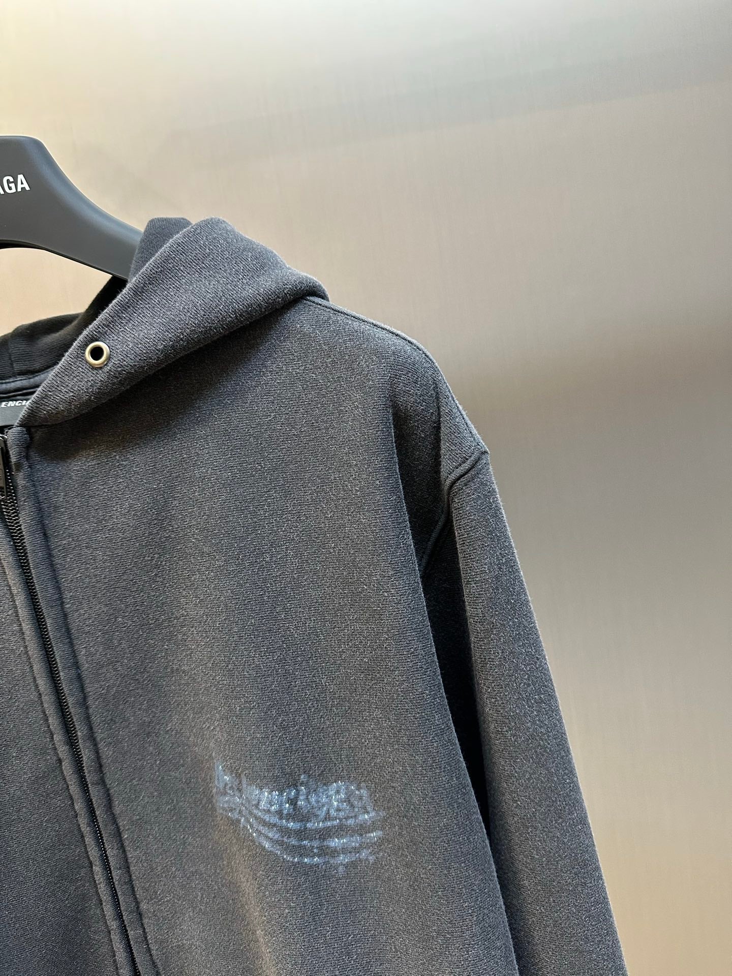 Dark gray zip hoodie with hood and button detail, arched logo print on chest