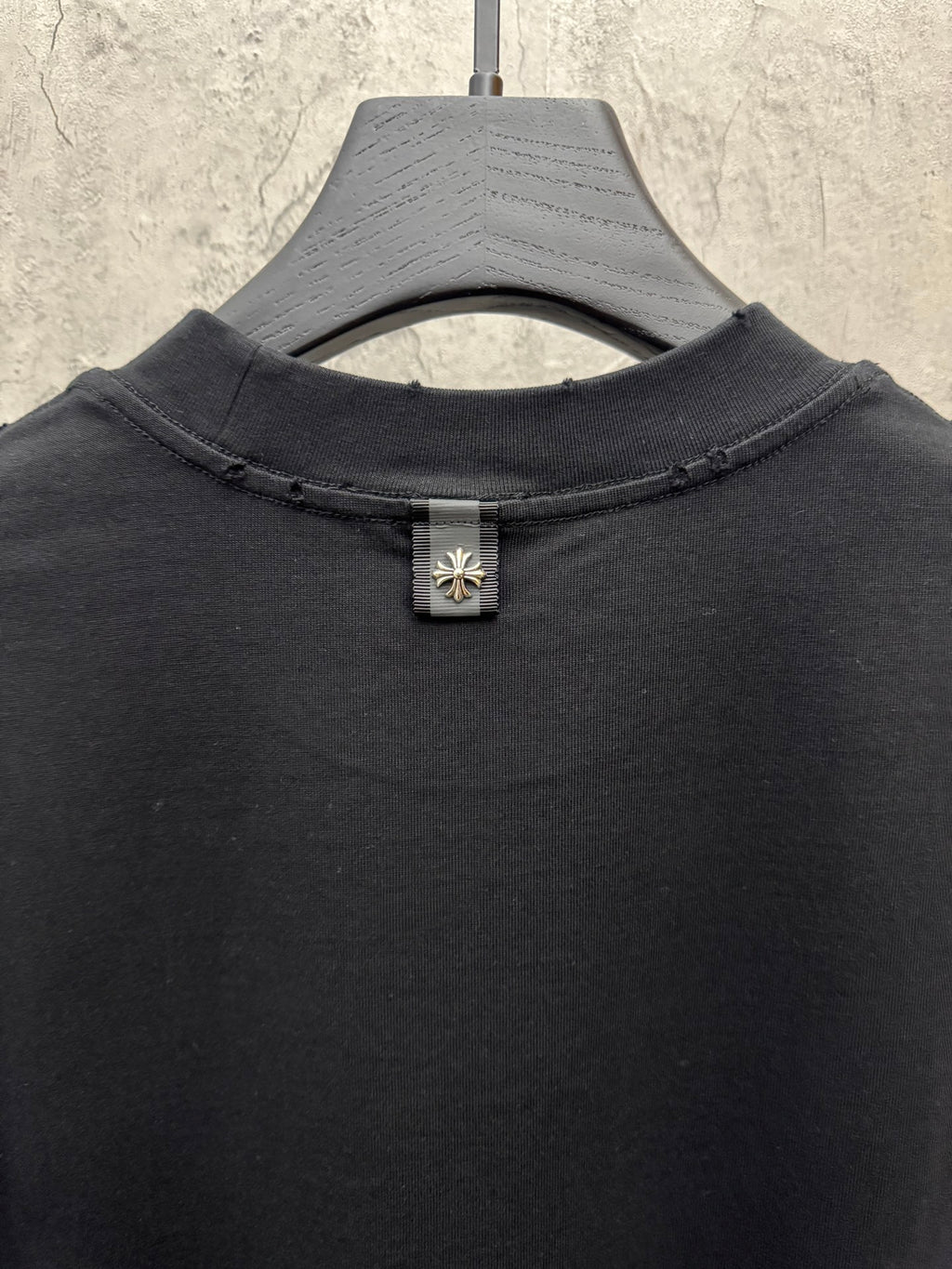 Black crewneck T-shirt close-up of neckline with small floral cross button detail