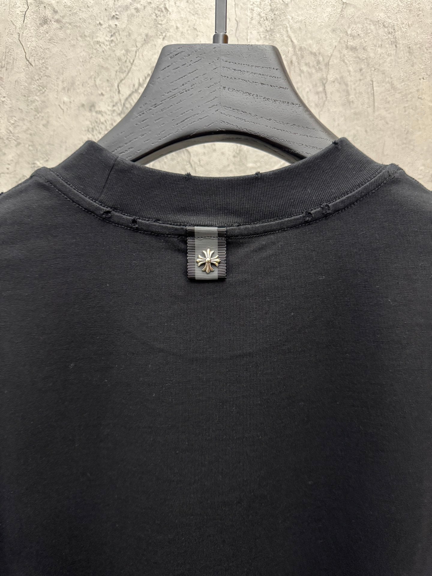 Black crewneck T-shirt close-up of neckline with small floral cross button detail
