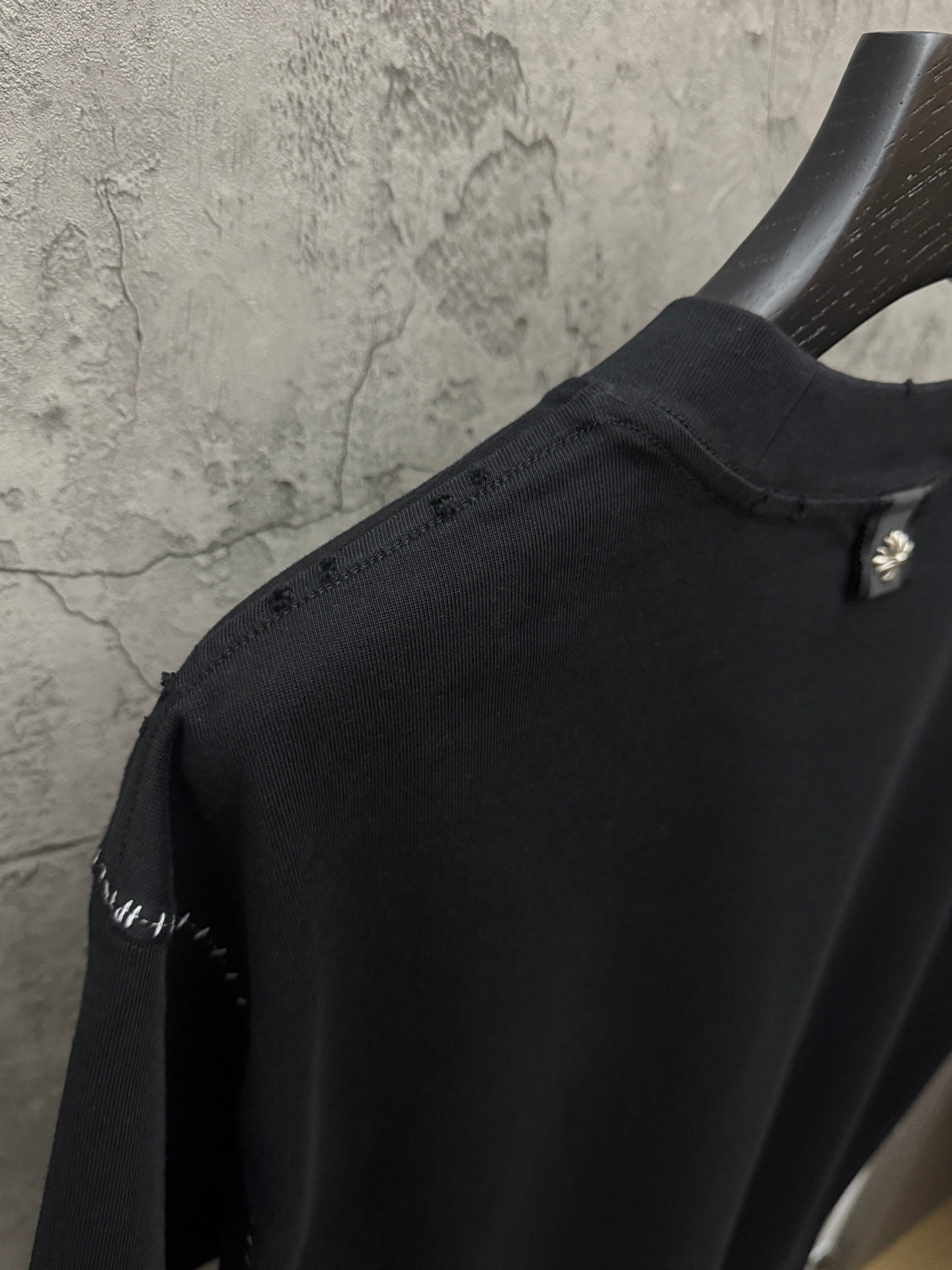 Black crewneck T-shirt close-up of shoulder and sleeve edge with stud trim