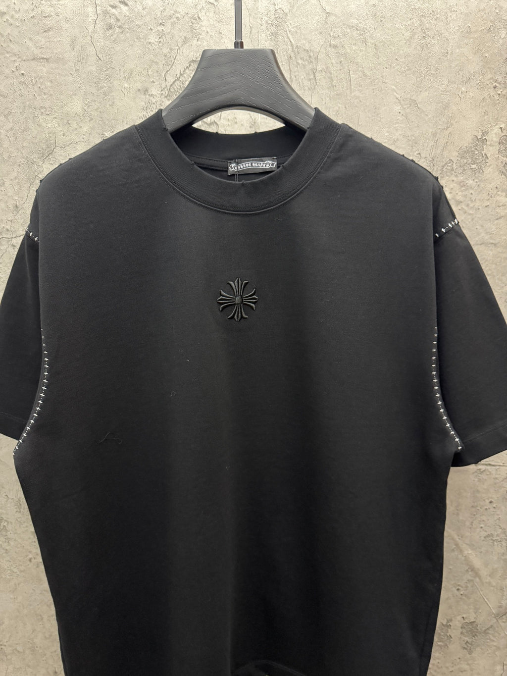 Black short-sleeve crewneck T-shirt with small floral cross emblem at center chest