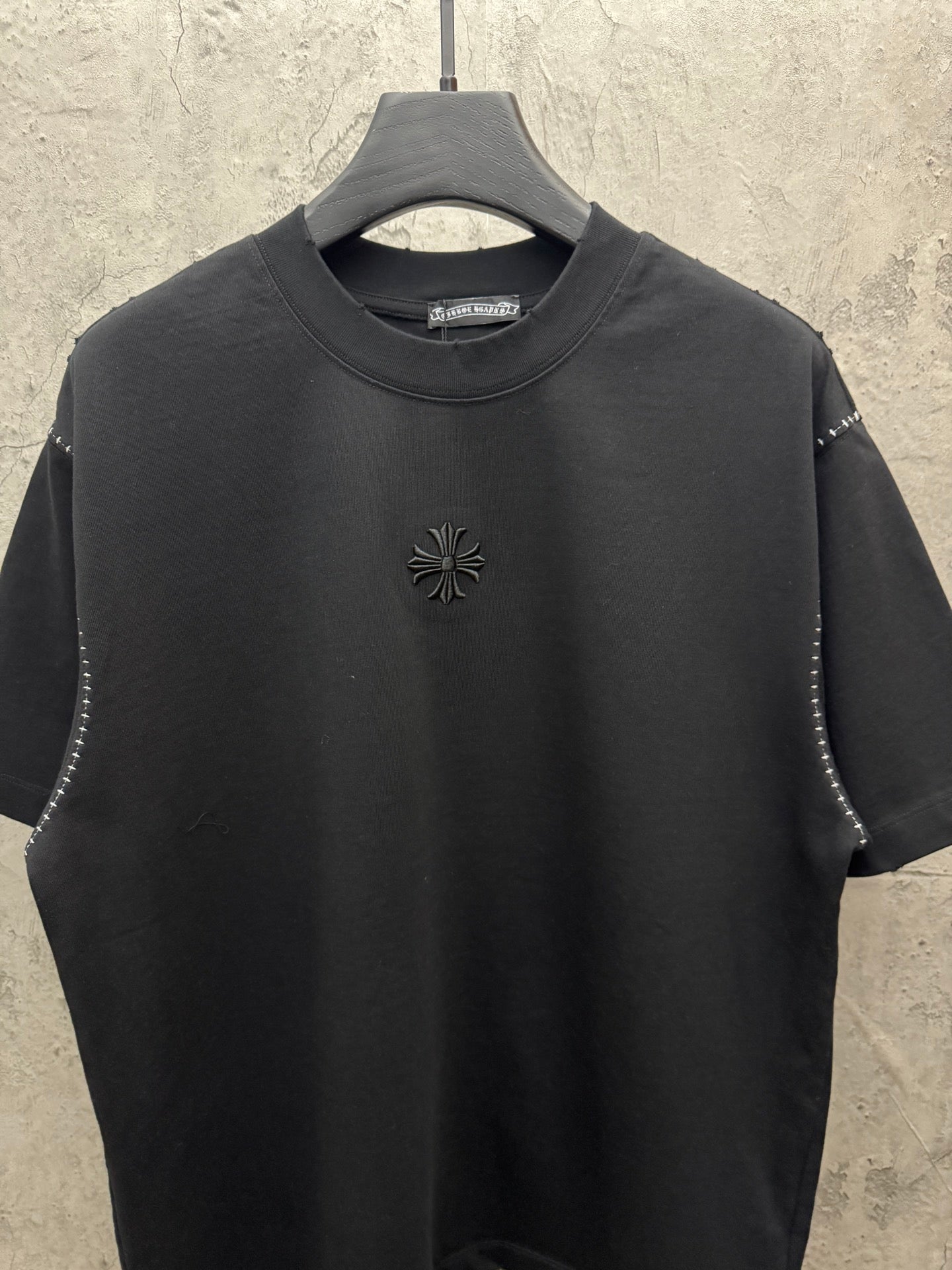 Black short-sleeve crewneck T-shirt with small floral cross emblem at center chest