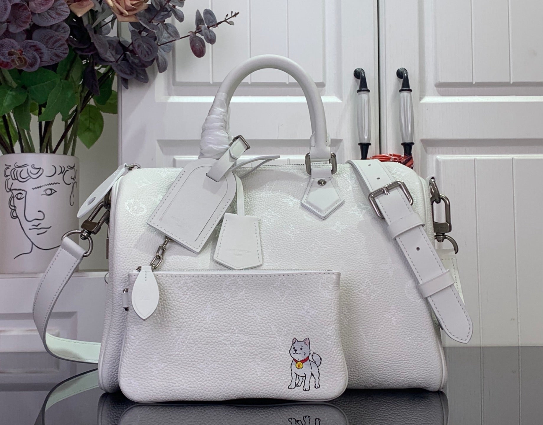 White leather handbag with top handles, crossbody strap, and front charm patch