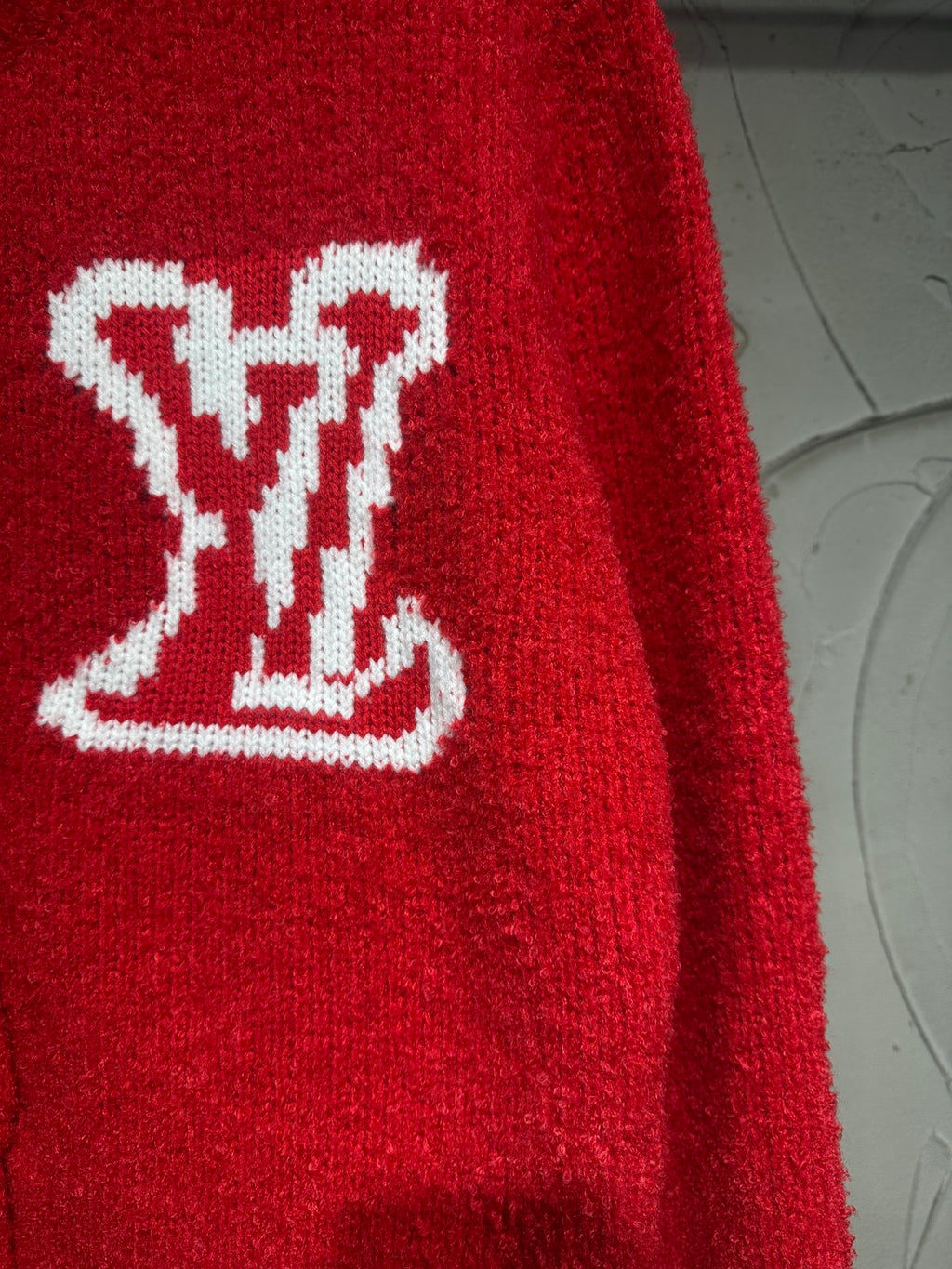 Red cardigan sleeve close-up with white LV-style logo graphic