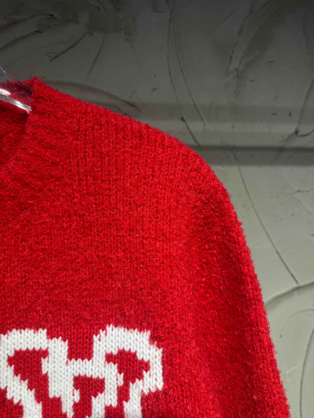 Red cardigan close-up of white LV-style intarsia logo on the sleeve