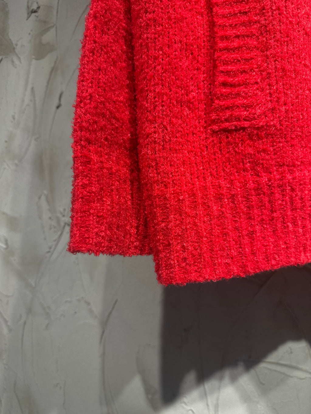 Red cardigan side view with ribbed hem and textured knit fabric