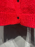 Red cardigan lower half close-up with black button and ribbed hem