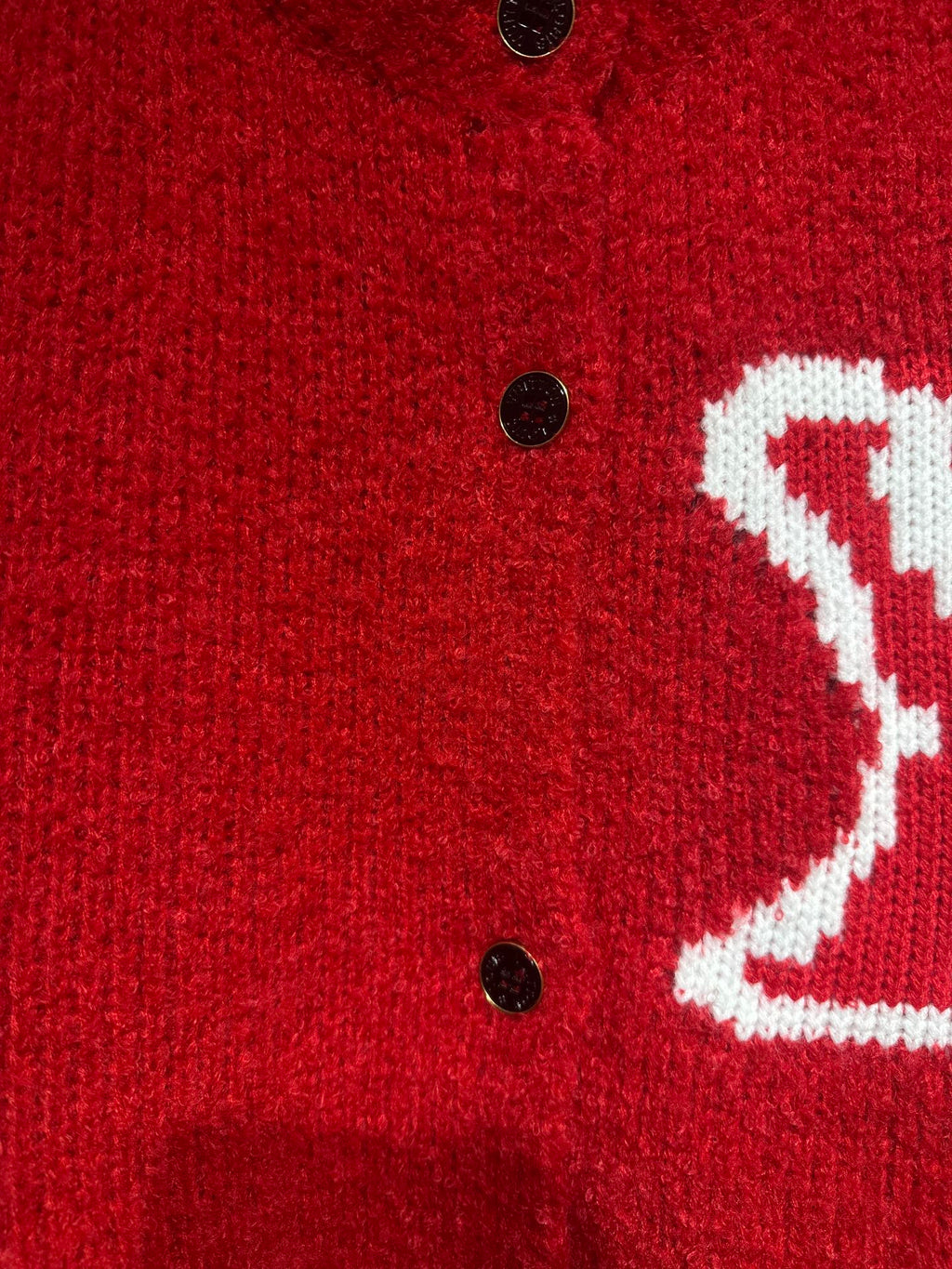 Red cardigan close-up of black buttons and partial white LV-style logo