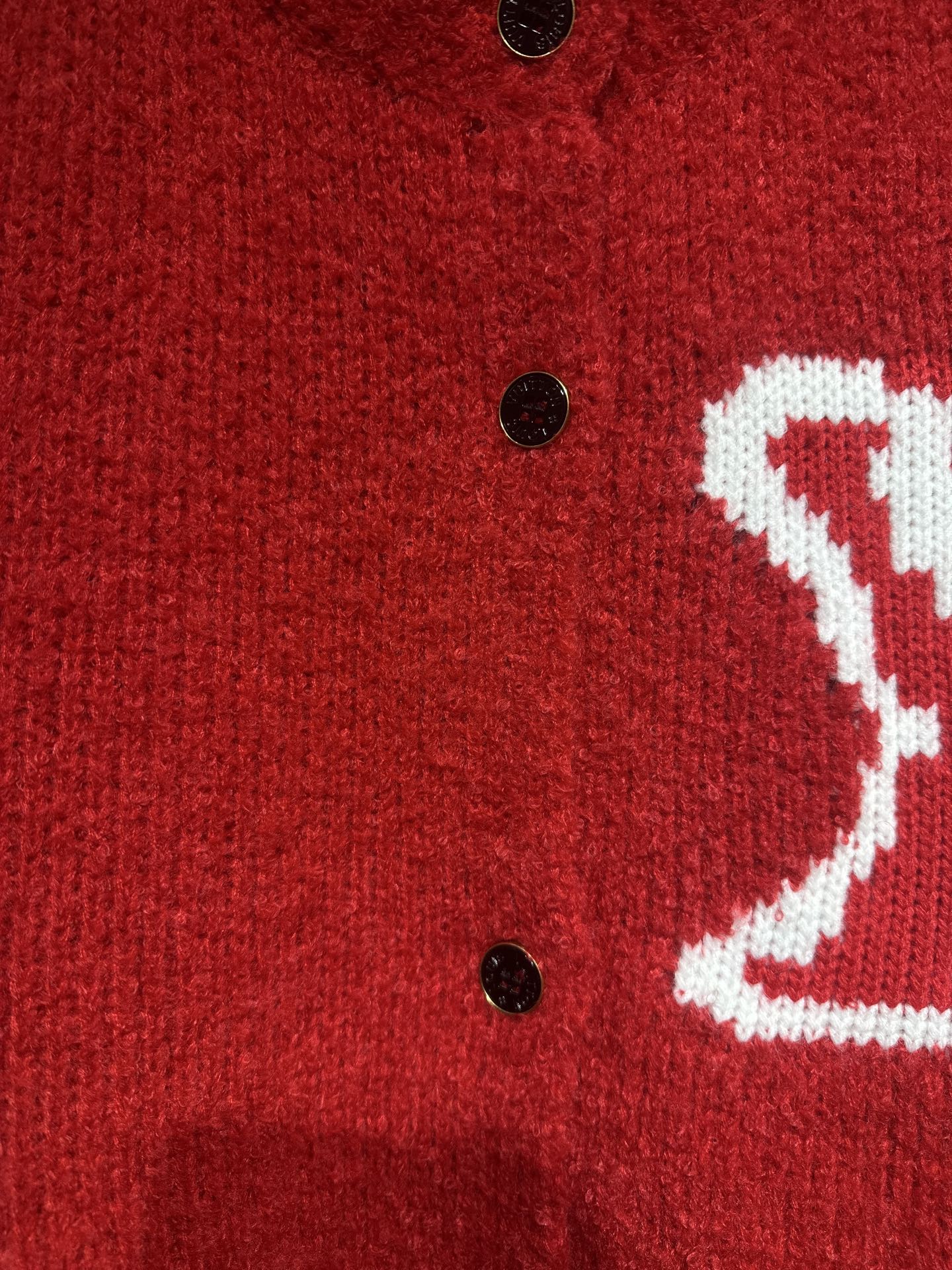 Red cardigan close-up of black buttons and partial white LV-style logo