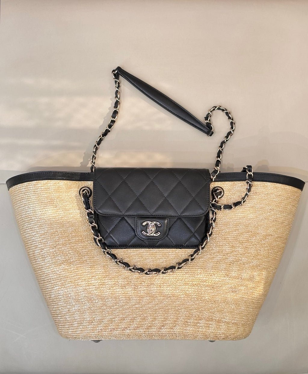 Beige woven tote bag with black trim, chain handles, and quilted flap mini bag