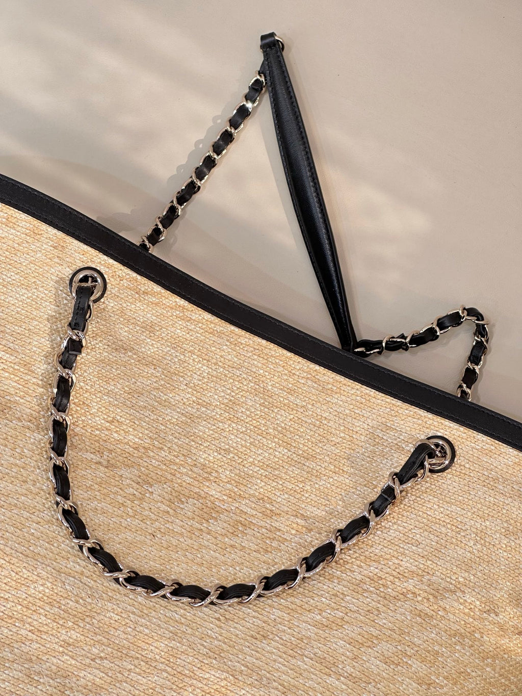 Beige woven tote bag corner view with chain handles and black top trim