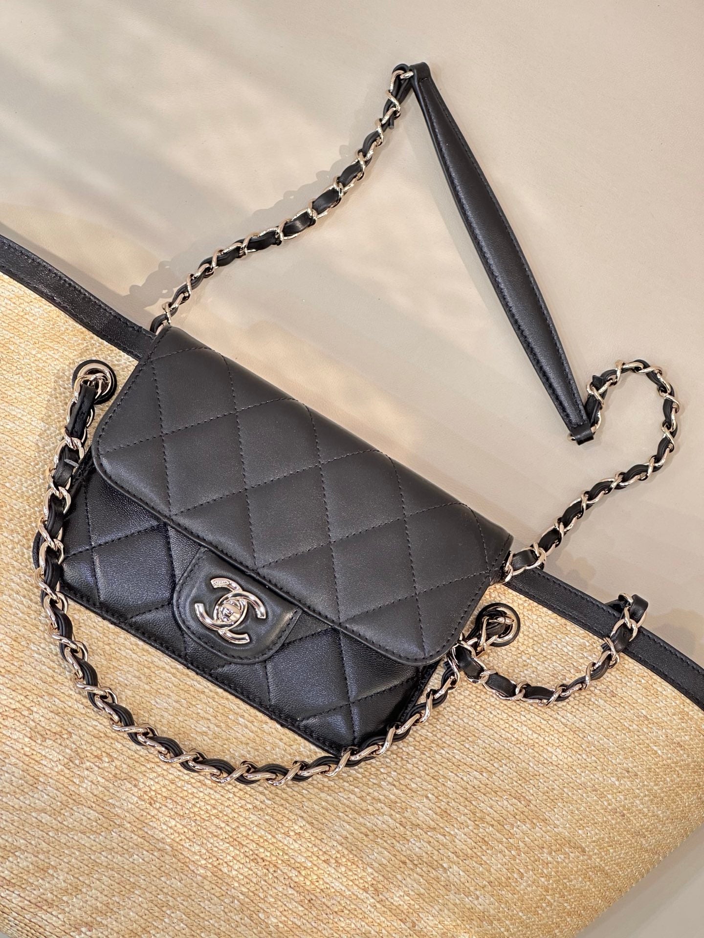 Black quilted mini bag with flap and chain strap on beige woven tote