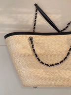 Beige woven tote bag with black chain handles and slim black top handle