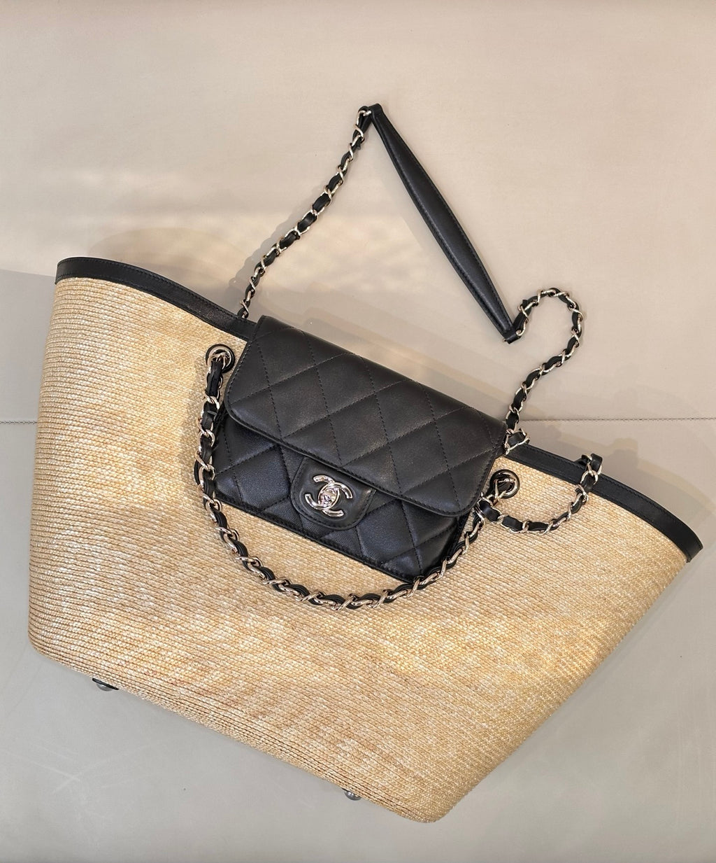 Beige woven tote bag with black trim, chain handles, and quilted crossbody