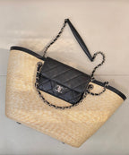 Beige woven tote bag with black trim, chain handles, and quilted crossbody