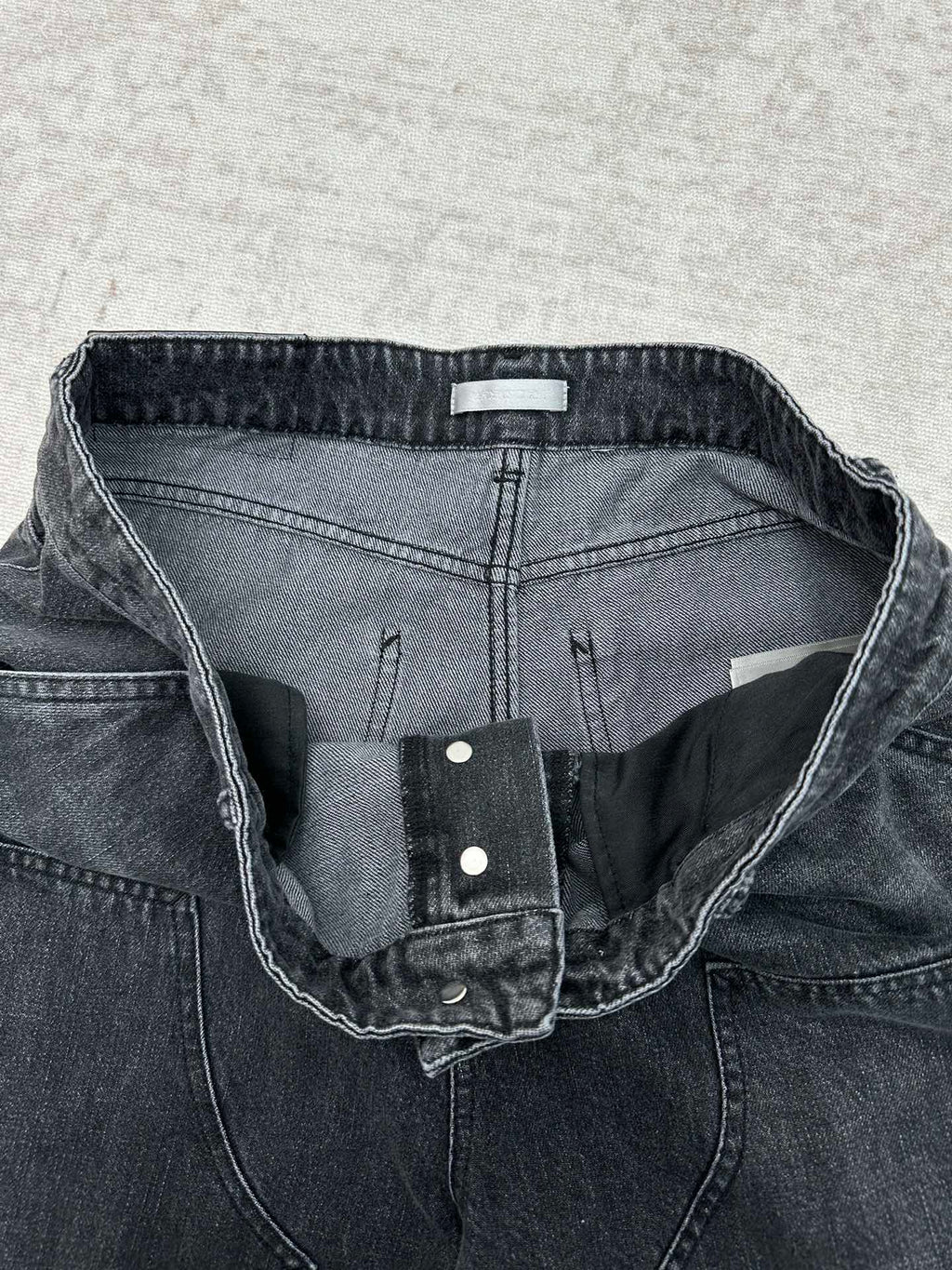 Denim pants waistband detail with inner label, snap closure, and stitched seams