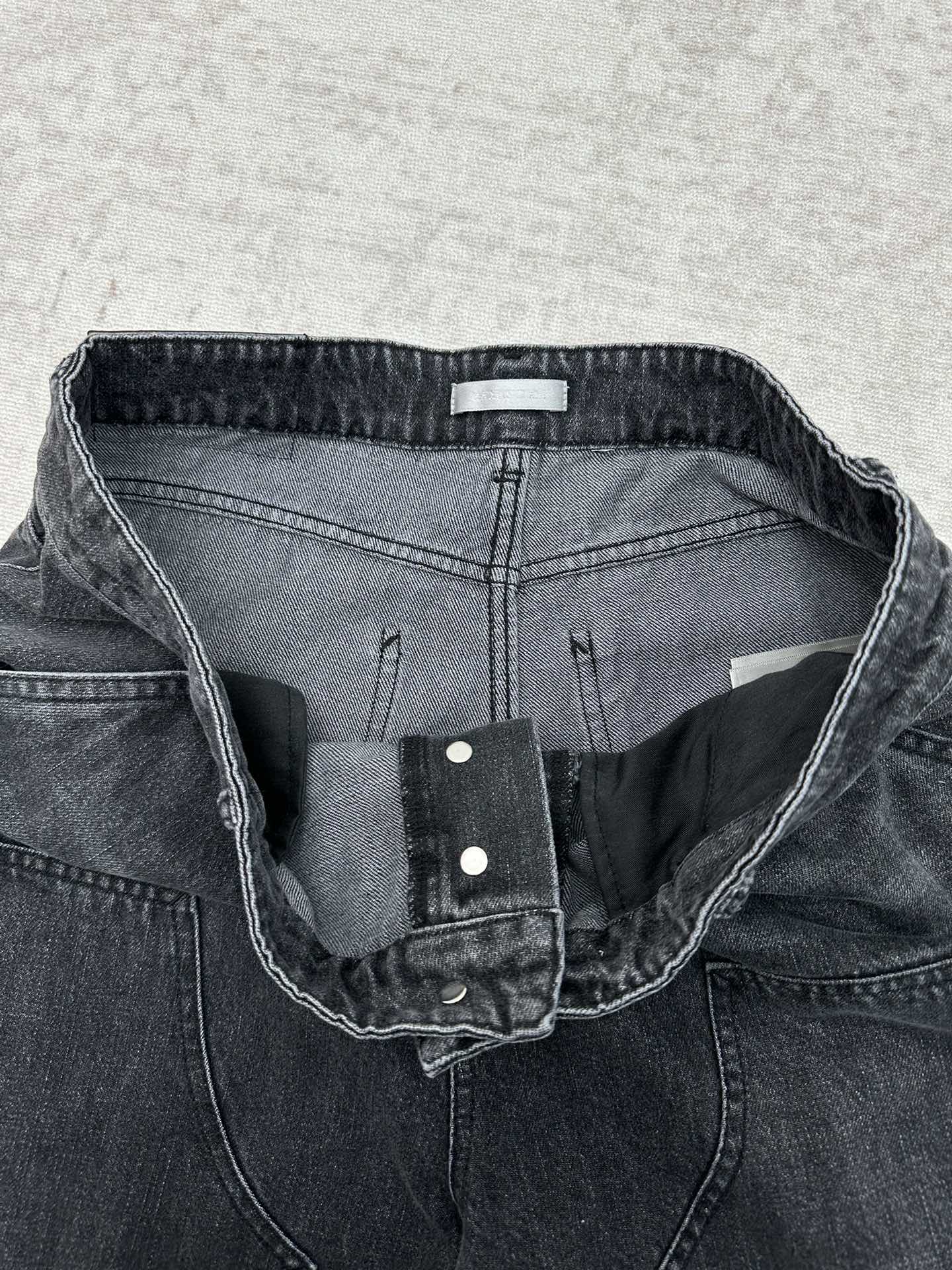 Denim pants waistband detail with inner label, snap closure, and stitched seams