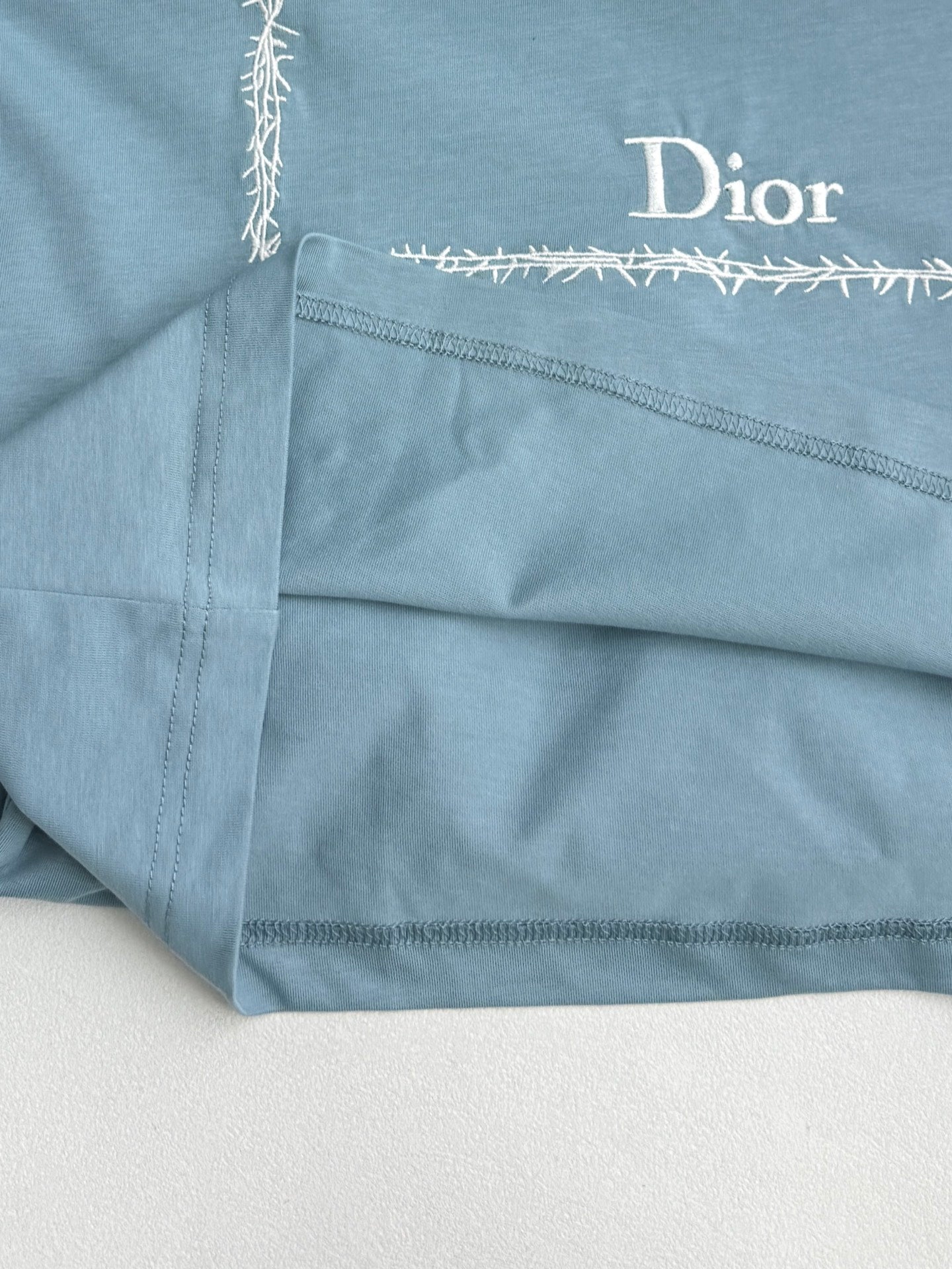 Light blue Dior T-shirt close-up of hem stitching and “Dior” label