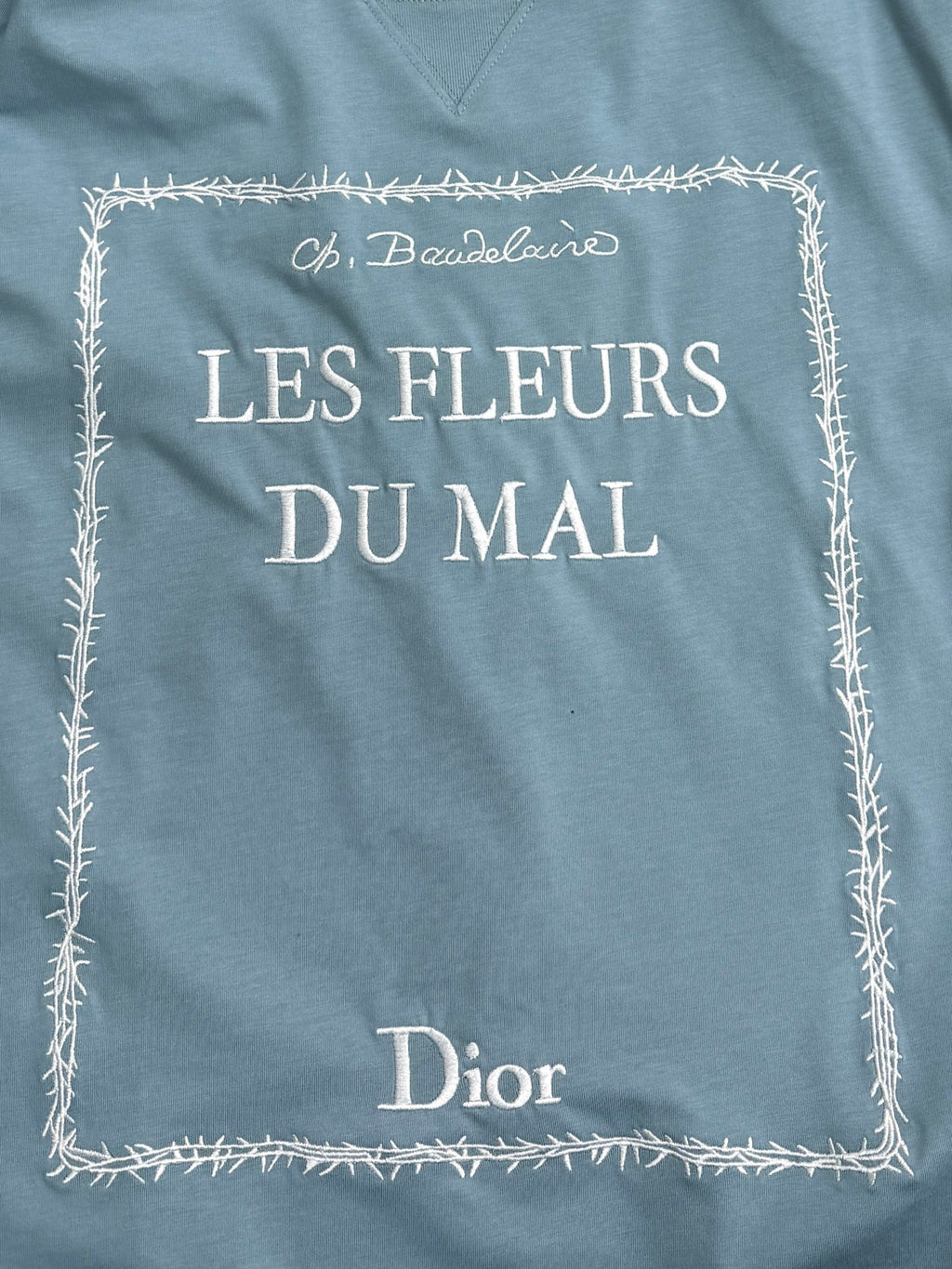 Light blue Dior T-shirt front: “LES FLEURS DU MAI” with decorative stitched border