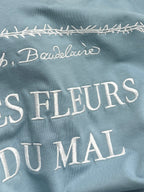 Light blue Dior T-shirt close-up of “LES FLEURS DU MAI” lettering and border stitch