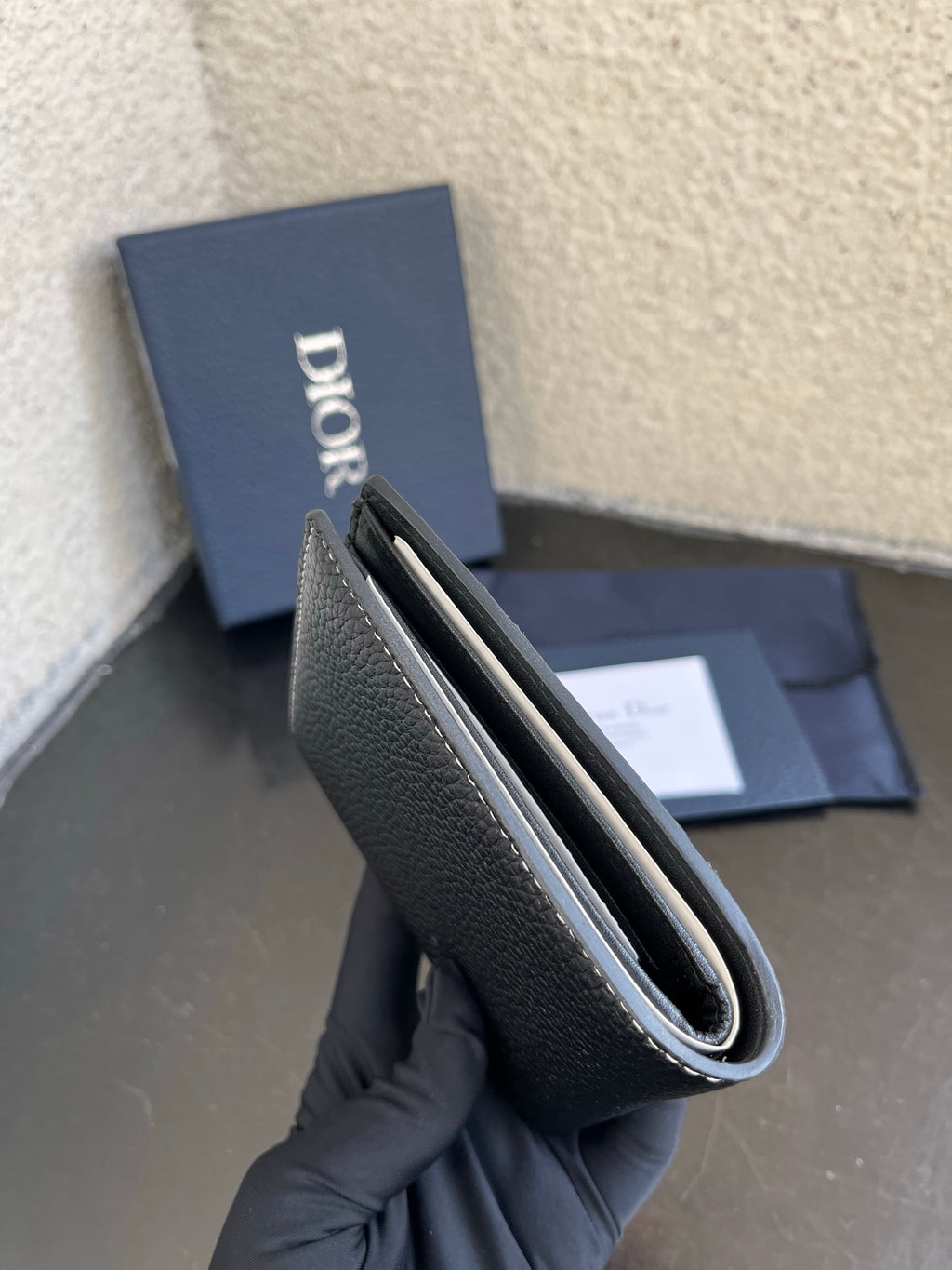 Dior small leather card wallet open view, textured dark exterior with inner card slots.