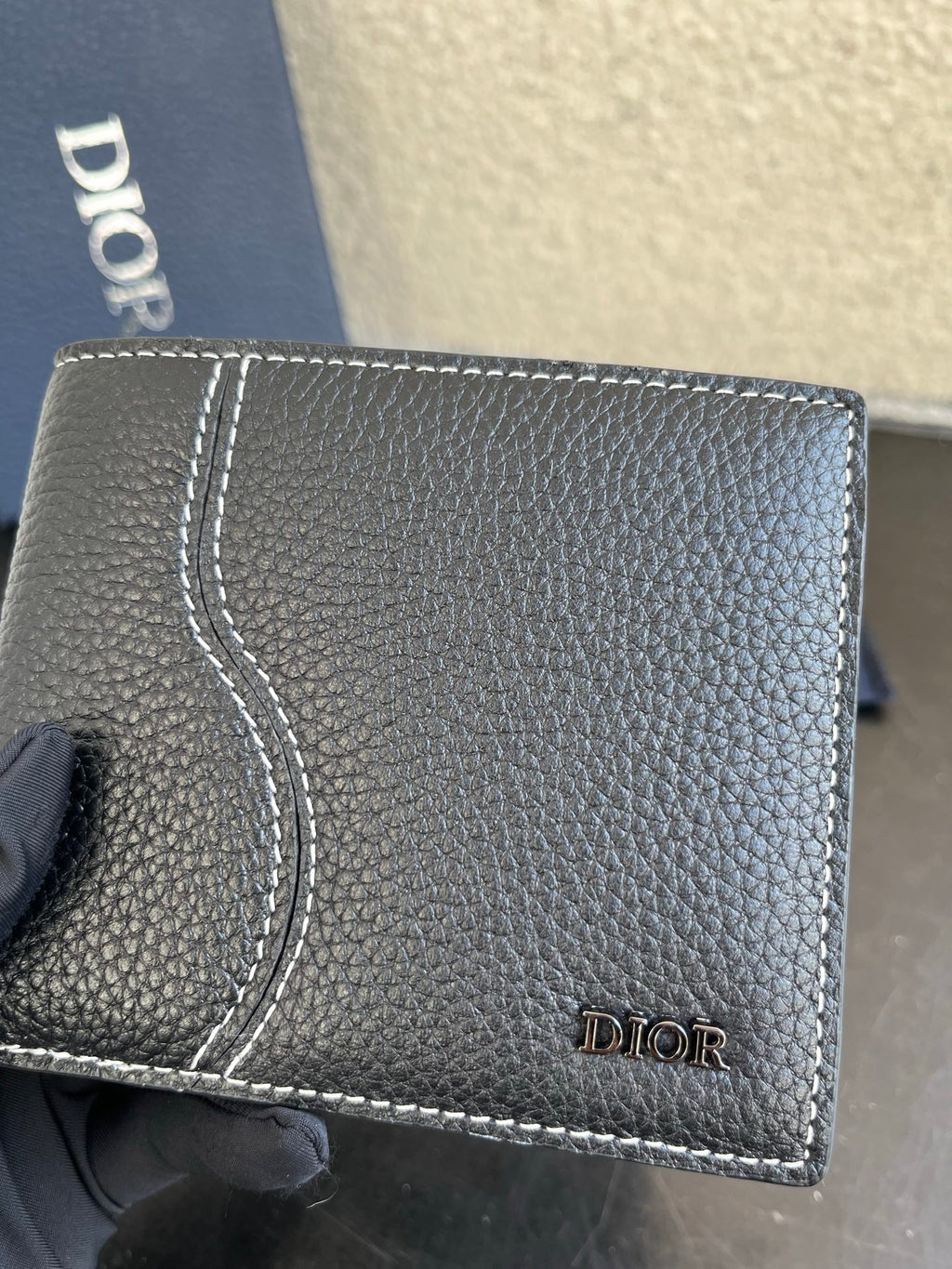 Dior small leather card wallet close-up, textured dark grain with stitched border and logo.
