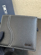 Dior small leather card wallet close-up, textured dark grain with stitched border and logo.